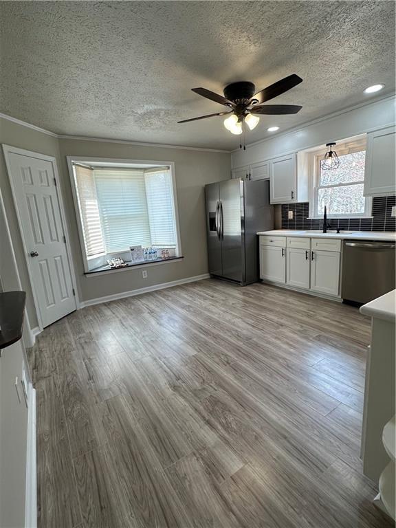 3967 Evelyn Dr, Powder Springs, GA 30127 - kitchen featuring crown molding, decorative backsplash, appliances with stainless steel finishes, light wood-style floors, and a ceiling fan