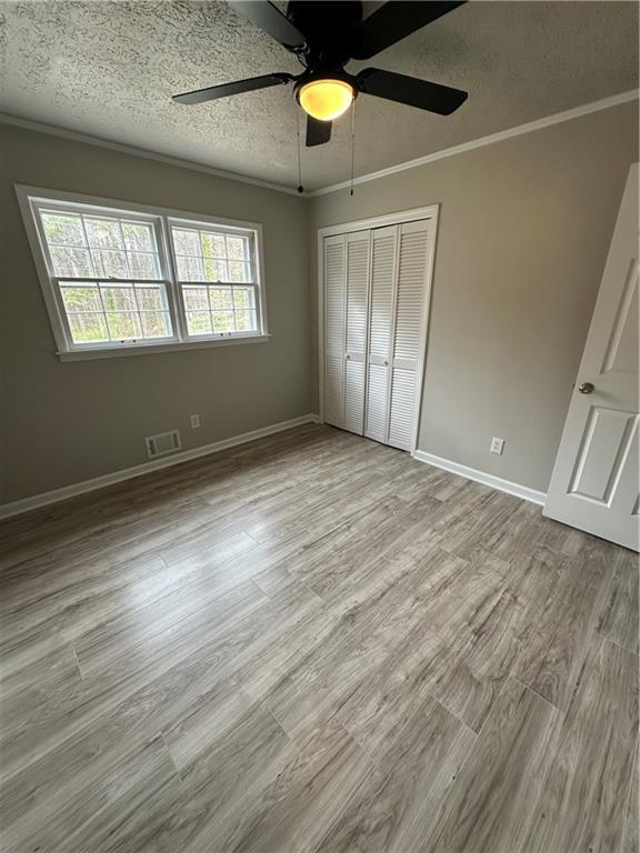 3967 Evelyn Dr, Powder Springs, GA 30127 - unfurnished bedroom with visible vents, a textured ceiling, crown molding, and wood finished floors