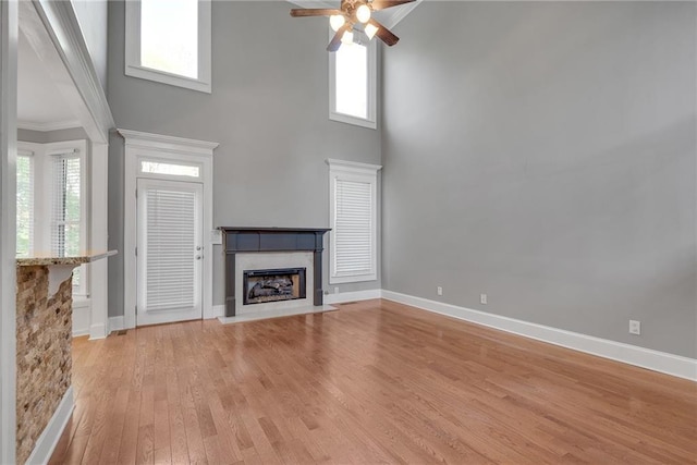 3085 Woodbridge Ln, Canton, GA 30114 - unfurnished living room featuring a towering ceiling, ceiling fan, light wood-style flooring, a fireplace with flush hearth, and baseboards