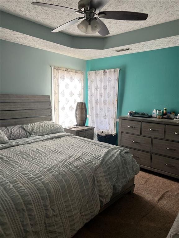 bedroom featuring a tray ceiling, a ceiling fan, a textured ceiling, and carpet flooring