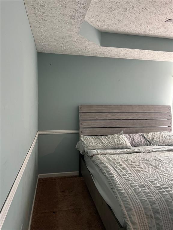 bedroom with a textured ceiling, dark colored carpet, and baseboards