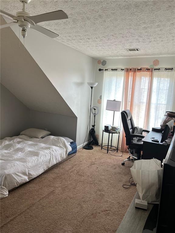 carpeted bedroom featuring a textured ceiling, ceiling fan, vaulted ceiling, and visible vents