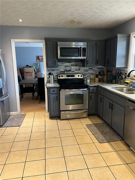 kitchen with light tile patterned floors, gray cabinets, stainless steel appliances, and a sink