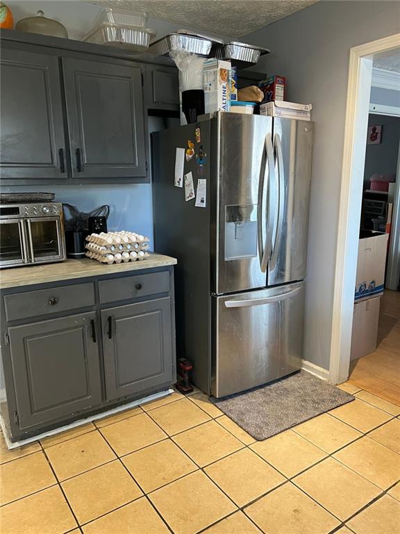 kitchen with light countertops, gray cabinets, light tile patterned flooring, and stainless steel fridge