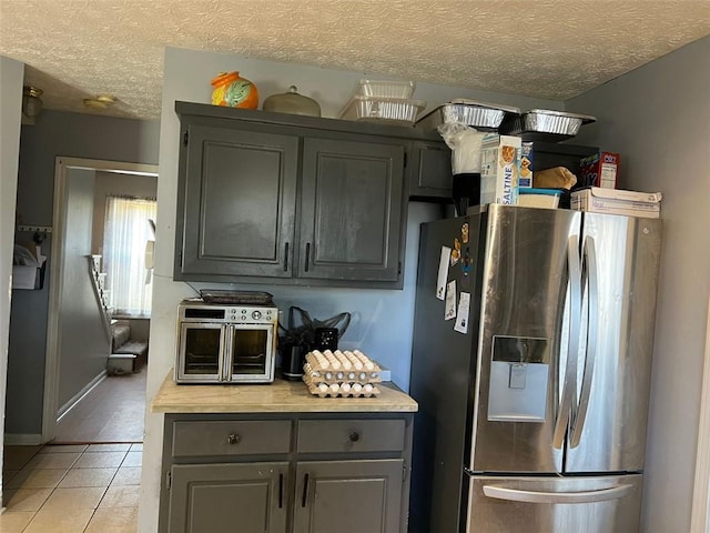 kitchen with gray cabinets, light countertops, light tile patterned flooring, a textured ceiling, and stainless steel fridge with ice dispenser