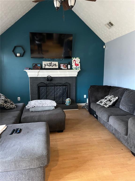 living area featuring visible vents, lofted ceiling, ceiling fan, wood finished floors, and a fireplace