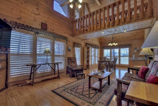 living room with light wood-type flooring, ceiling fan with notable chandelier, high vaulted ceiling, and wood walls