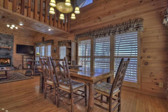 dining area with wood walls, light hardwood / wood-style floors, a high ceiling, and an inviting chandelier