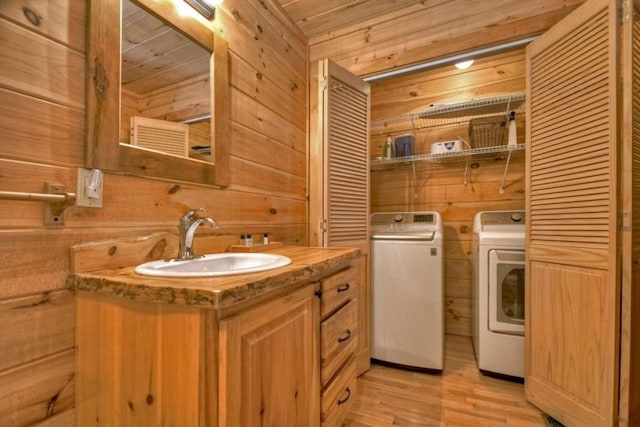 washroom featuring wooden walls, washer and dryer, light hardwood / wood-style floors, wooden ceiling, and sink