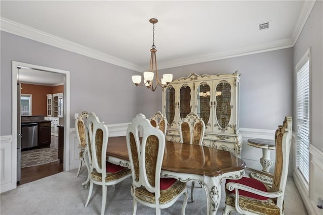 dining space with a notable chandelier, crown molding, and light colored carpet