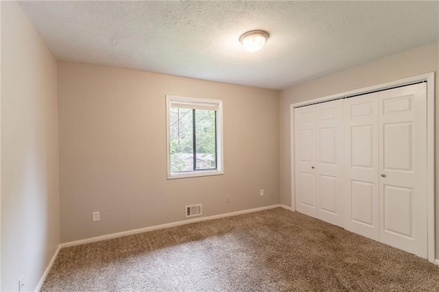unfurnished bedroom featuring a closet, a textured ceiling, carpet, baseboards, and visible vents