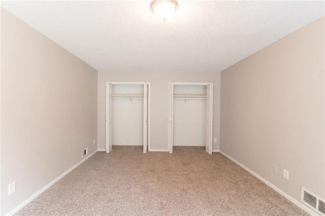 unfurnished bedroom with a textured ceiling, multiple closets, visible vents, and light colored carpet