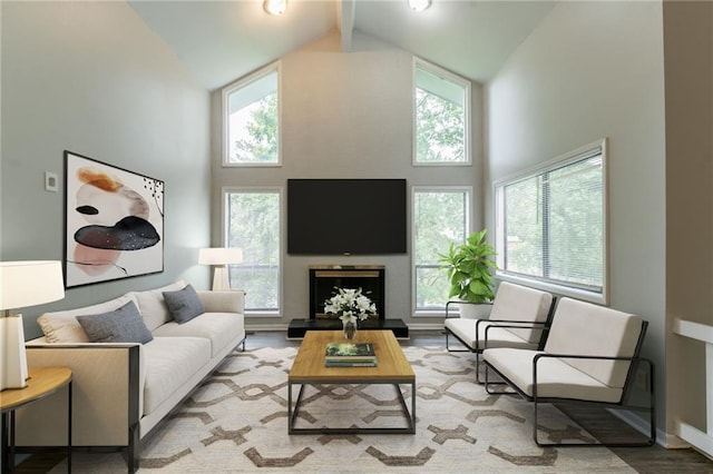 living room featuring baseboards, high vaulted ceiling, a fireplace with raised hearth, and wood finished floors