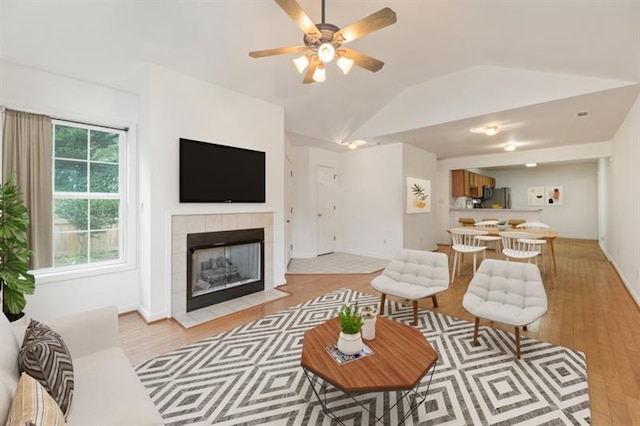 living room with light wood-type flooring, ceiling fan, lofted ceiling, and a tiled fireplace