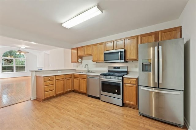 kitchen with ceiling fan, sink, stainless steel appliances, kitchen peninsula, and light hardwood / wood-style floors