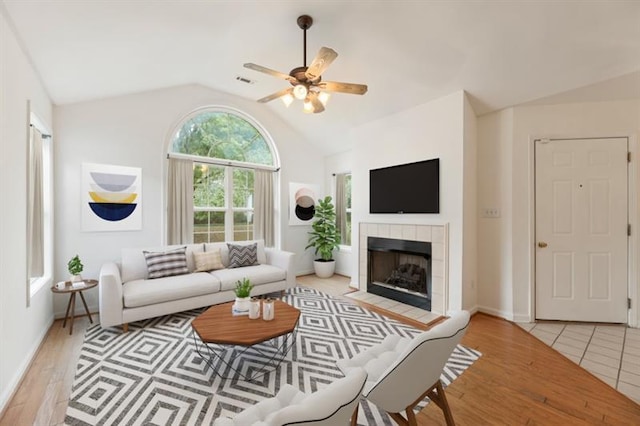 living room featuring vaulted ceiling, light hardwood / wood-style flooring, ceiling fan, and a tiled fireplace