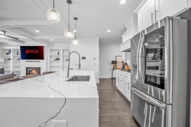 kitchen with a kitchen island with sink, a fireplace, a sink, white cabinets, and stainless steel refrigerator with ice dispenser