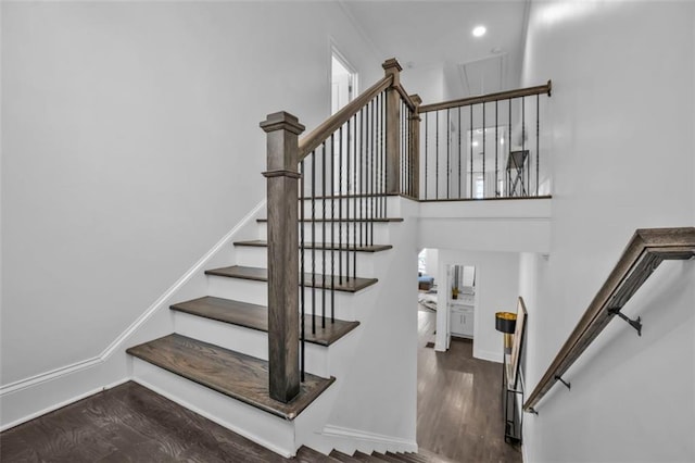 staircase with a towering ceiling, baseboards, and wood finished floors