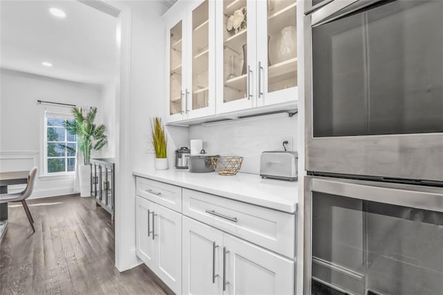 kitchen featuring dark wood-style floors, double oven, glass insert cabinets, and white cabinetry