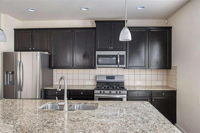 kitchen featuring light stone counters, backsplash, stainless steel appliances, sink, and decorative light fixtures