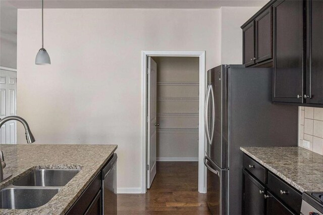 kitchen with dark wood-type flooring, dark brown cabinets, sink, decorative light fixtures, and light stone counters