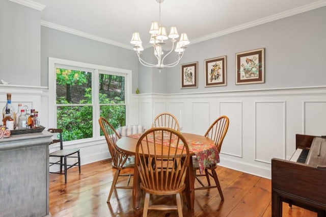 dining area featuring a decorative wall, a chandelier, ornamental molding, light wood-style floors, and wainscoting