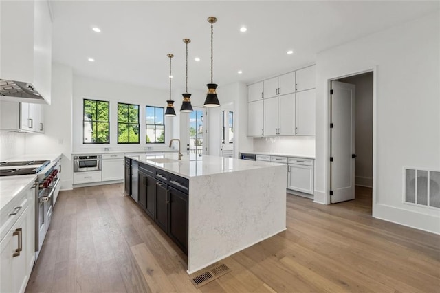 12632 Branyan Cir, Alpharetta, GA 30004 - kitchen with wall chimney exhaust hood, range with two ovens, white cabinets, light wood-type flooring, and a center island with sink