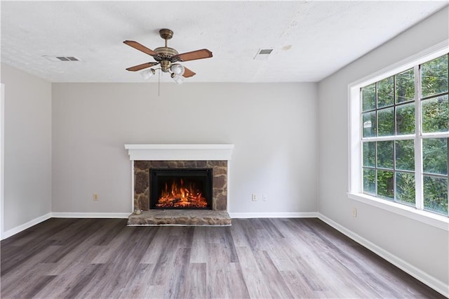 unfurnished living room featuring dark wood-type flooring, ceiling fan, and a stone fireplace