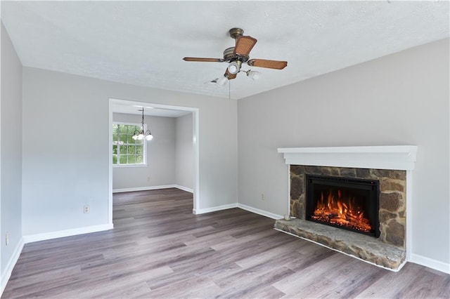 unfurnished living room featuring a fireplace, ceiling fan with notable chandelier, and wood-type flooring