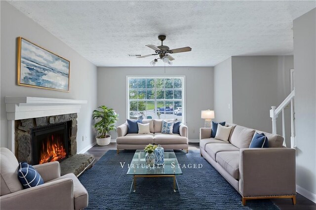 living room featuring a textured ceiling, dark wood-type flooring, ceiling fan, and a fireplace