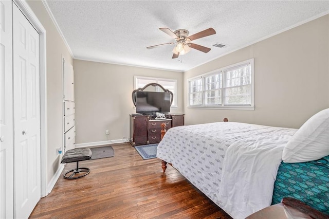 bedroom featuring wood finished floors, baseboards, visible vents, a textured ceiling, and crown molding