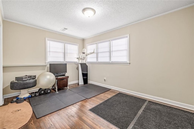 exercise room featuring visible vents, baseboards, wood finished floors, and crown molding