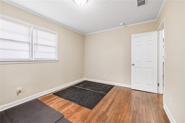 empty room featuring visible vents, baseboards, wood finished floors, and ornamental molding