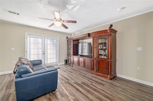 living room featuring visible vents, ornamental molding, a textured ceiling, wood finished floors, and baseboards