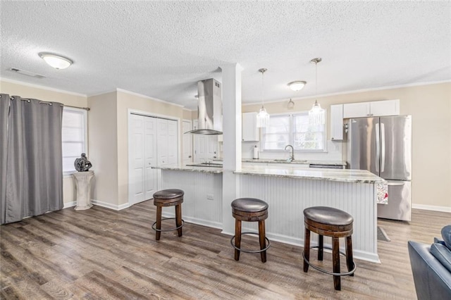 kitchen featuring ventilation hood, wood finished floors, freestanding refrigerator, a sink, and a kitchen breakfast bar