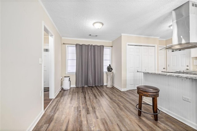 interior space with a breakfast bar area, dark wood-type flooring, wall chimney exhaust hood, and ornamental molding