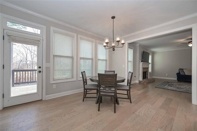 dining space featuring crown molding, ceiling fan with notable chandelier, a fireplace, and light hardwood / wood-style floors