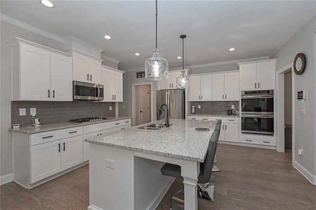 kitchen featuring appliances with stainless steel finishes, decorative light fixtures, white cabinetry, an island with sink, and sink