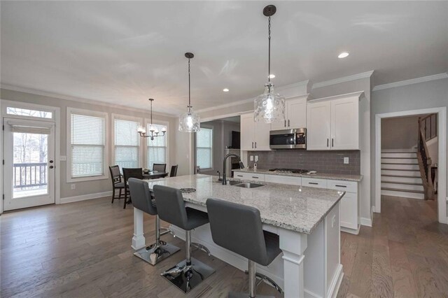 kitchen featuring pendant lighting, white cabinetry, sink, gas cooktop, and a center island with sink