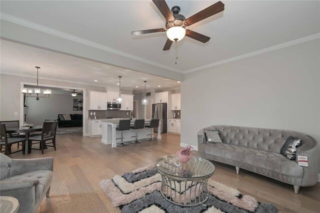 living room with crown molding, ceiling fan with notable chandelier, and light hardwood / wood-style floors