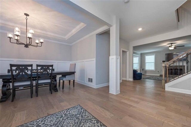 dining area with crown molding, hardwood / wood-style flooring, ceiling fan with notable chandelier, and a raised ceiling