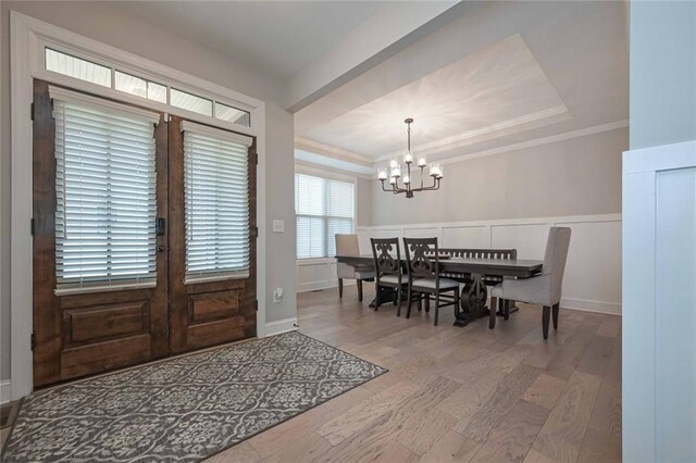 entryway with a chandelier, ornamental molding, a raised ceiling, and hardwood / wood-style floors