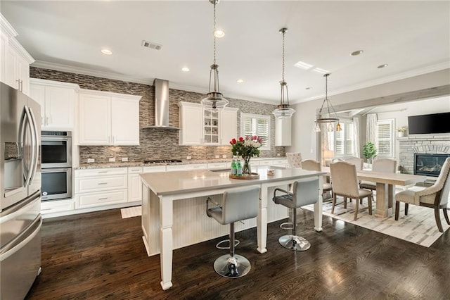 kitchen featuring wall chimney range hood, visible vents, appliances with stainless steel finishes, light countertops, and dark wood-style floors