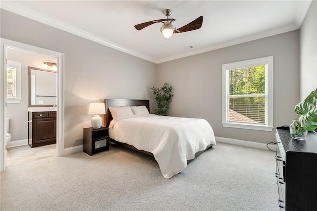 bedroom featuring crown molding, baseboards, ensuite bathroom, light colored carpet, and a ceiling fan