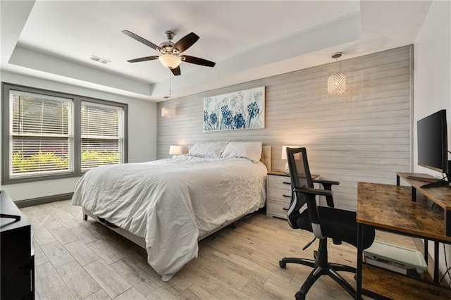 bedroom with baseboards, a tray ceiling, light wood finished floors, and visible vents