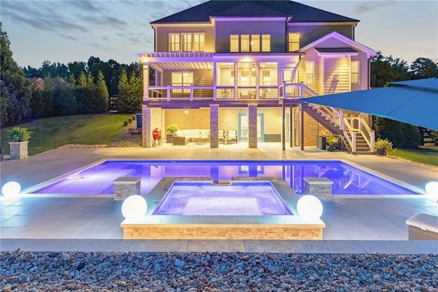 rear view of property with stairs, outdoor lounge area, an outdoor pool, an in ground hot tub, and a patio