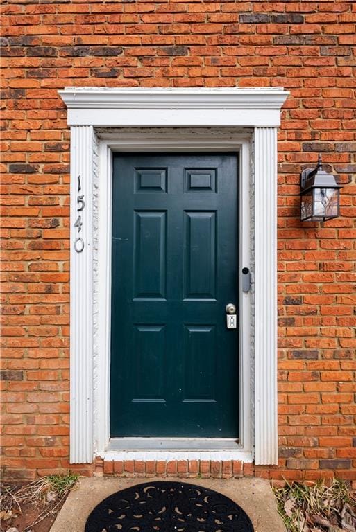 doorway to property featuring a shingled roof and brick siding