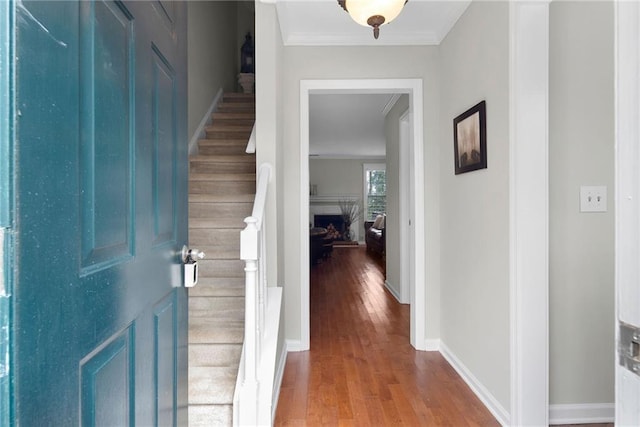 foyer entrance featuring a premium fireplace, wood finished floors, baseboards, stairs, and crown molding