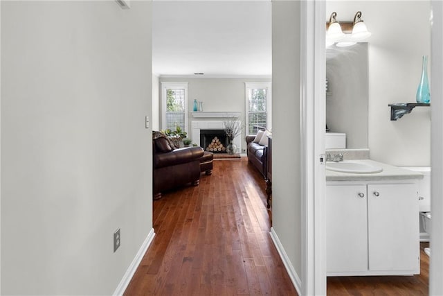 corridor with dark wood-type flooring, a sink, and baseboards