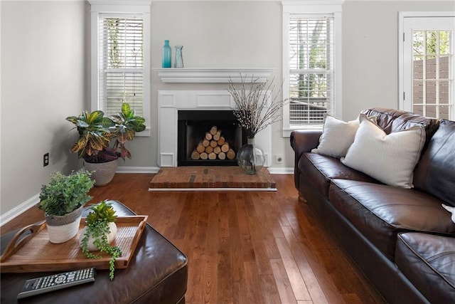 living area with a fireplace with raised hearth, hardwood / wood-style floors, and a healthy amount of sunlight